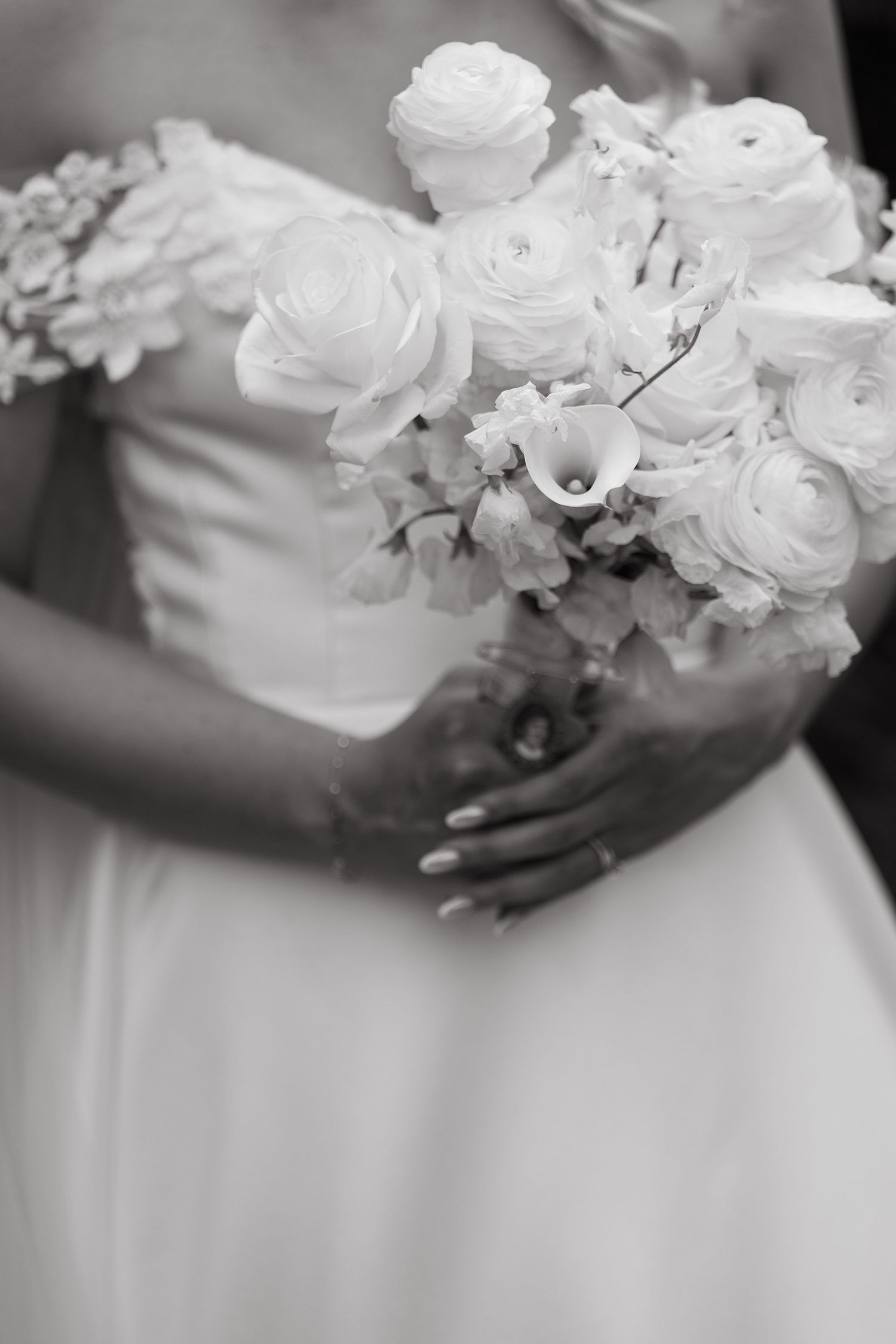 Black and white wedding photo showing white roses in a bridal bouquet against a flowing white dress.