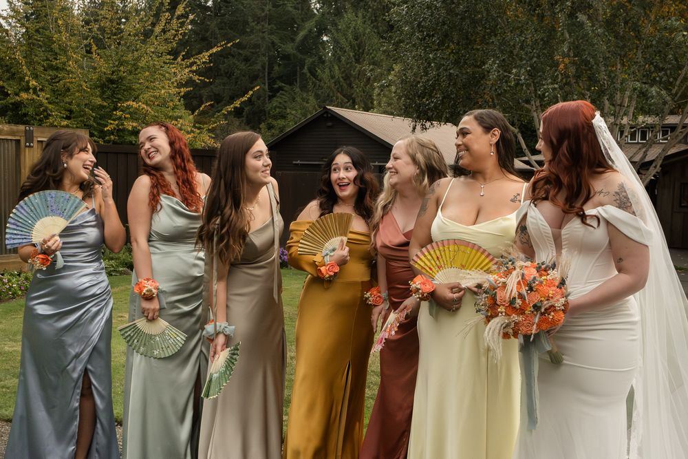 Wedding party wearing mix of gray and yellow dresses poses with autumn bouquets in outdoor setting.
