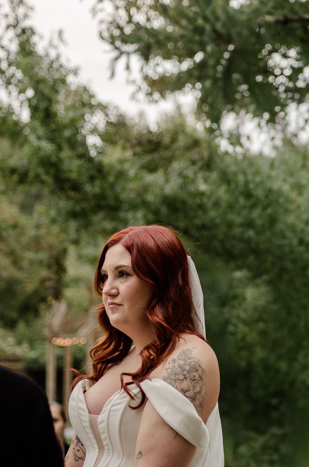 A bride in a white dress with red hair poses outdoors against a natural green background.