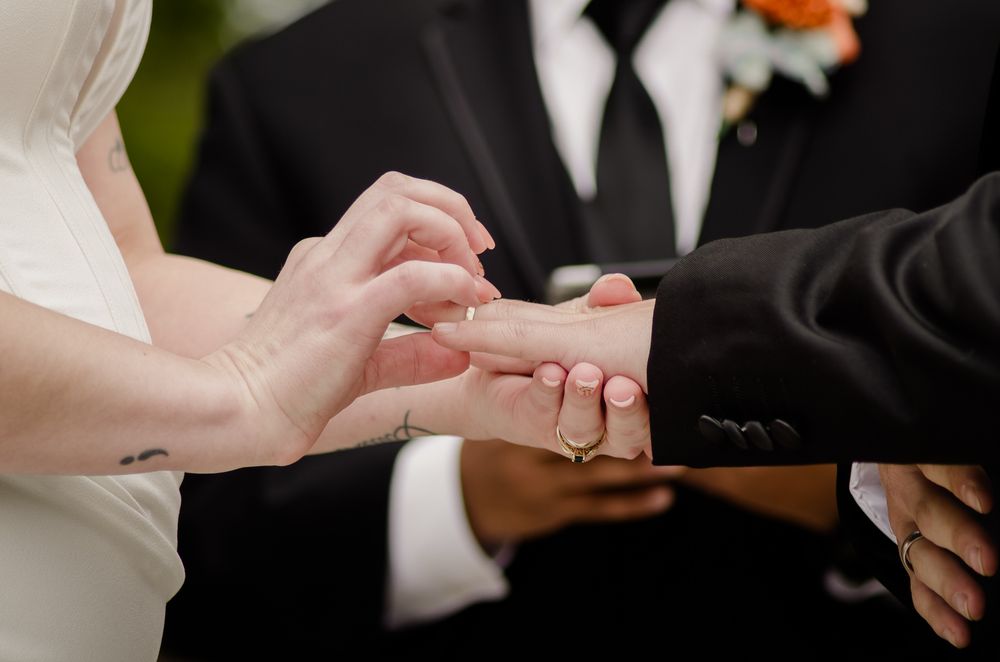 A close-up of wedding rings being exchanged during a ceremony with orange floral accents visible.