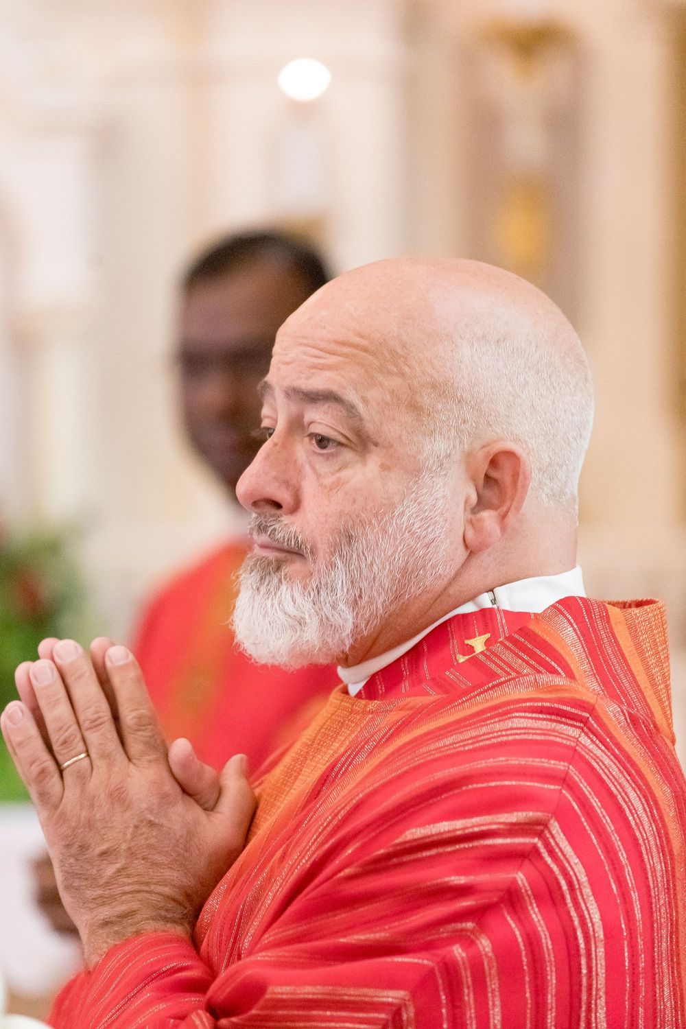 Mike Castanza in red religious vestments praying with hands clasped during a Red Mass.