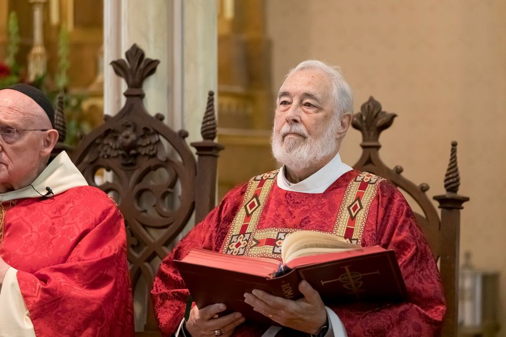 Religious ceremony with clergy in red vestments at ornate church altar.