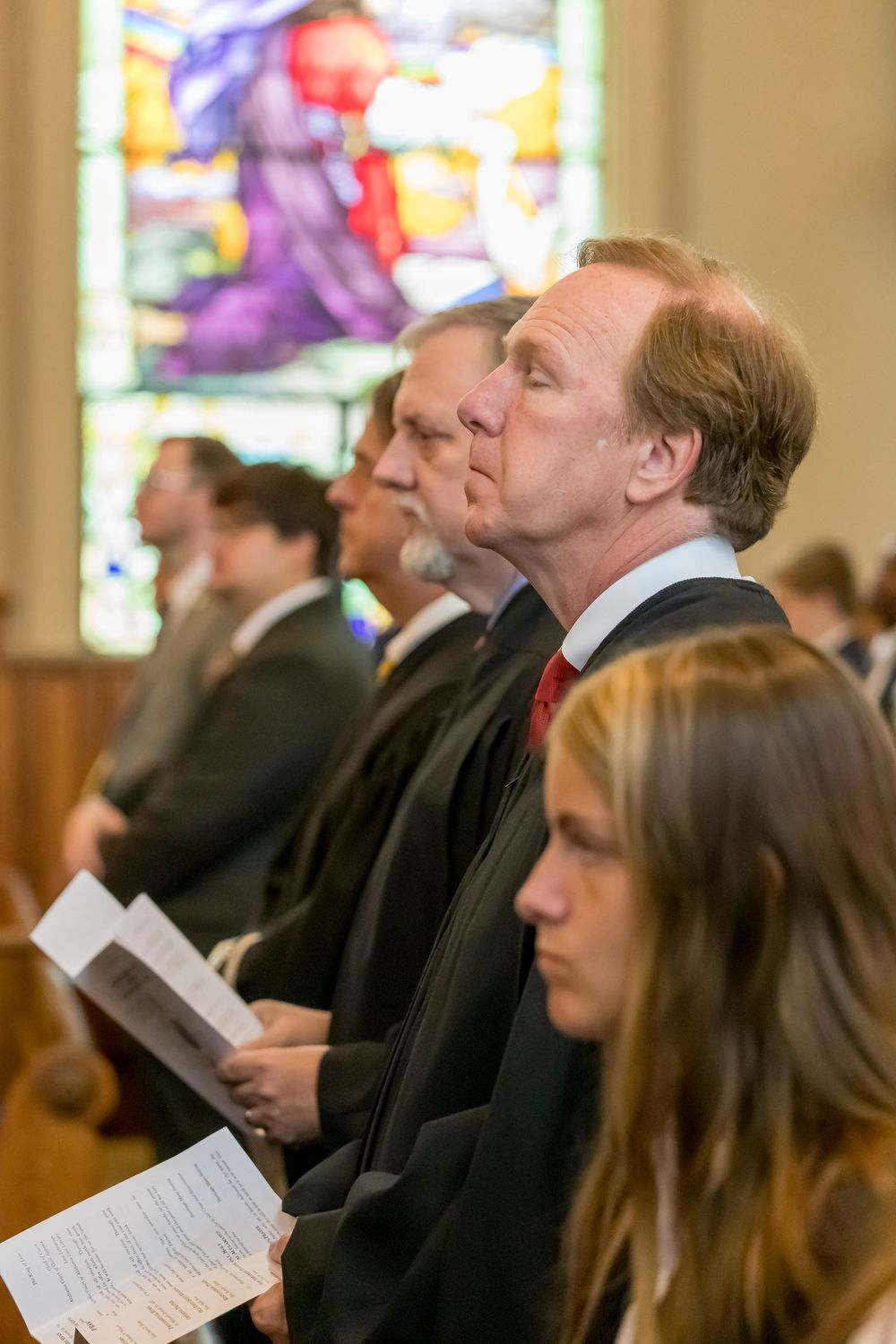 Attendees in formal attire seated in church pews during ceremonial event.