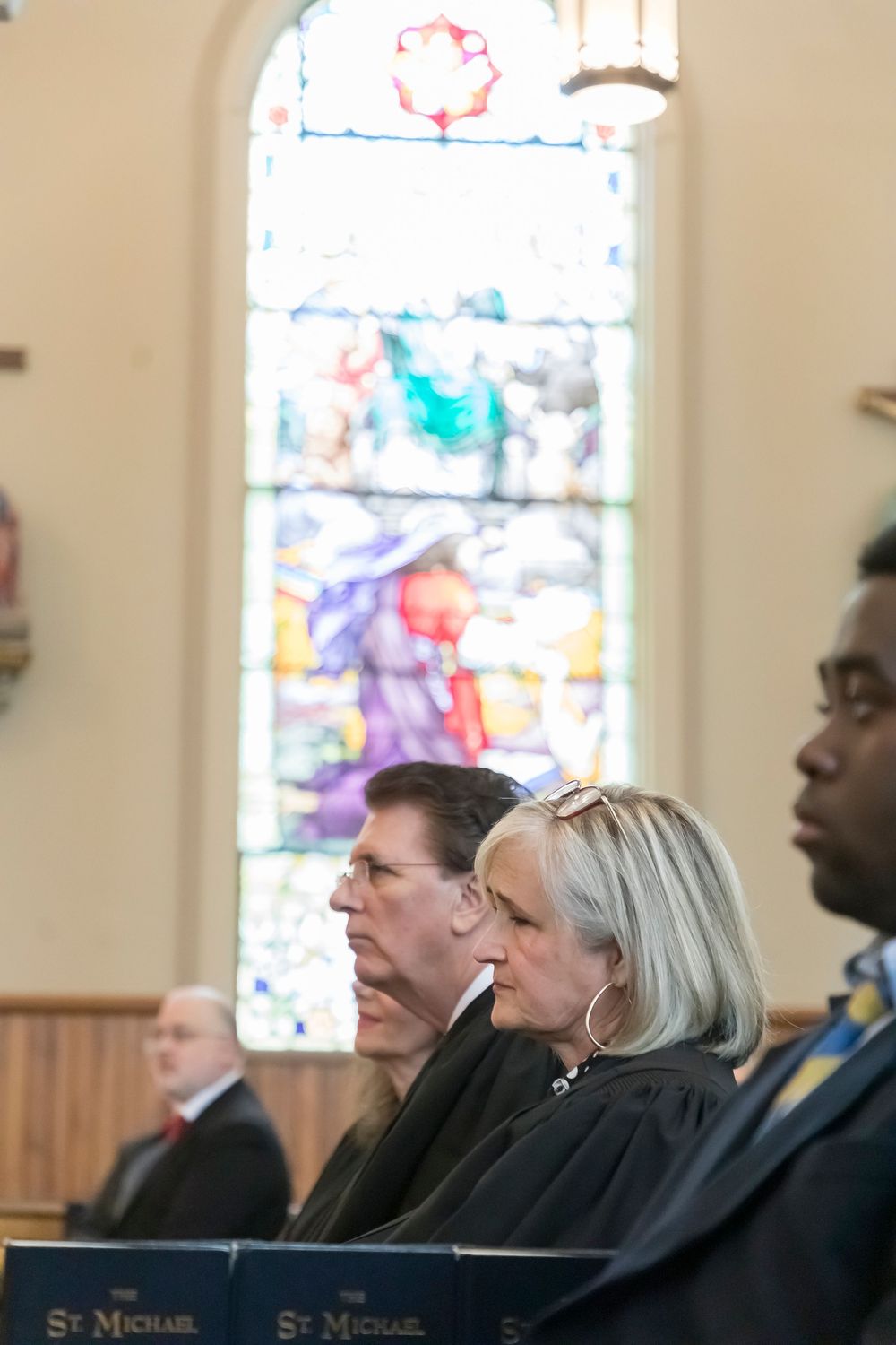 Chief Justice Sarah Hicks Stewart and Justice Tommy Elias Bryan seated at Red Mass with colorful stained glass in background.