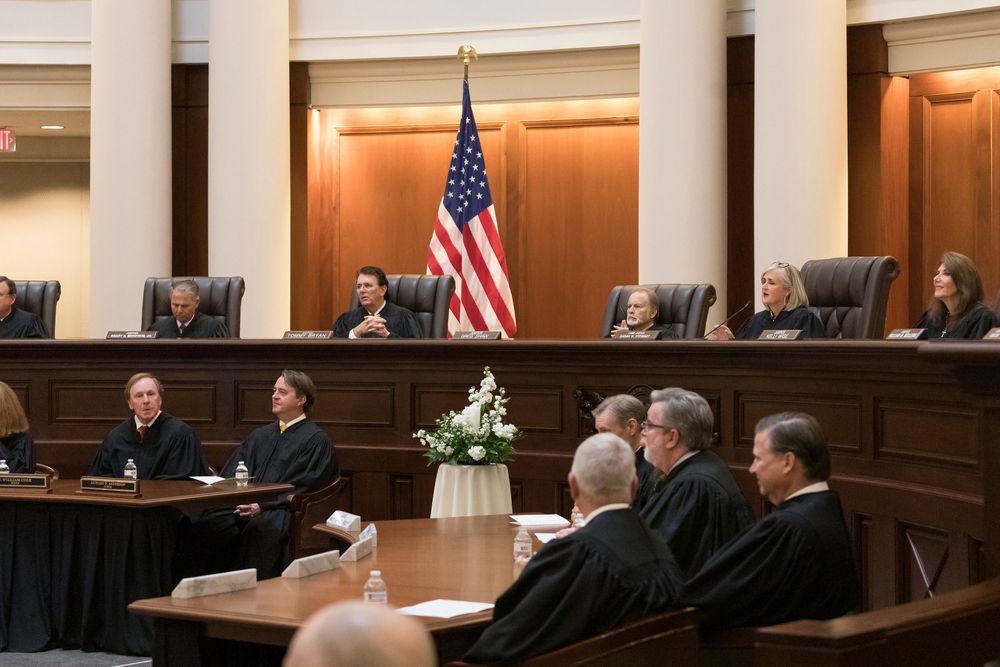View of a formal courtroom with wooden furnishings, American flag, and black robed figures seated at the bench.