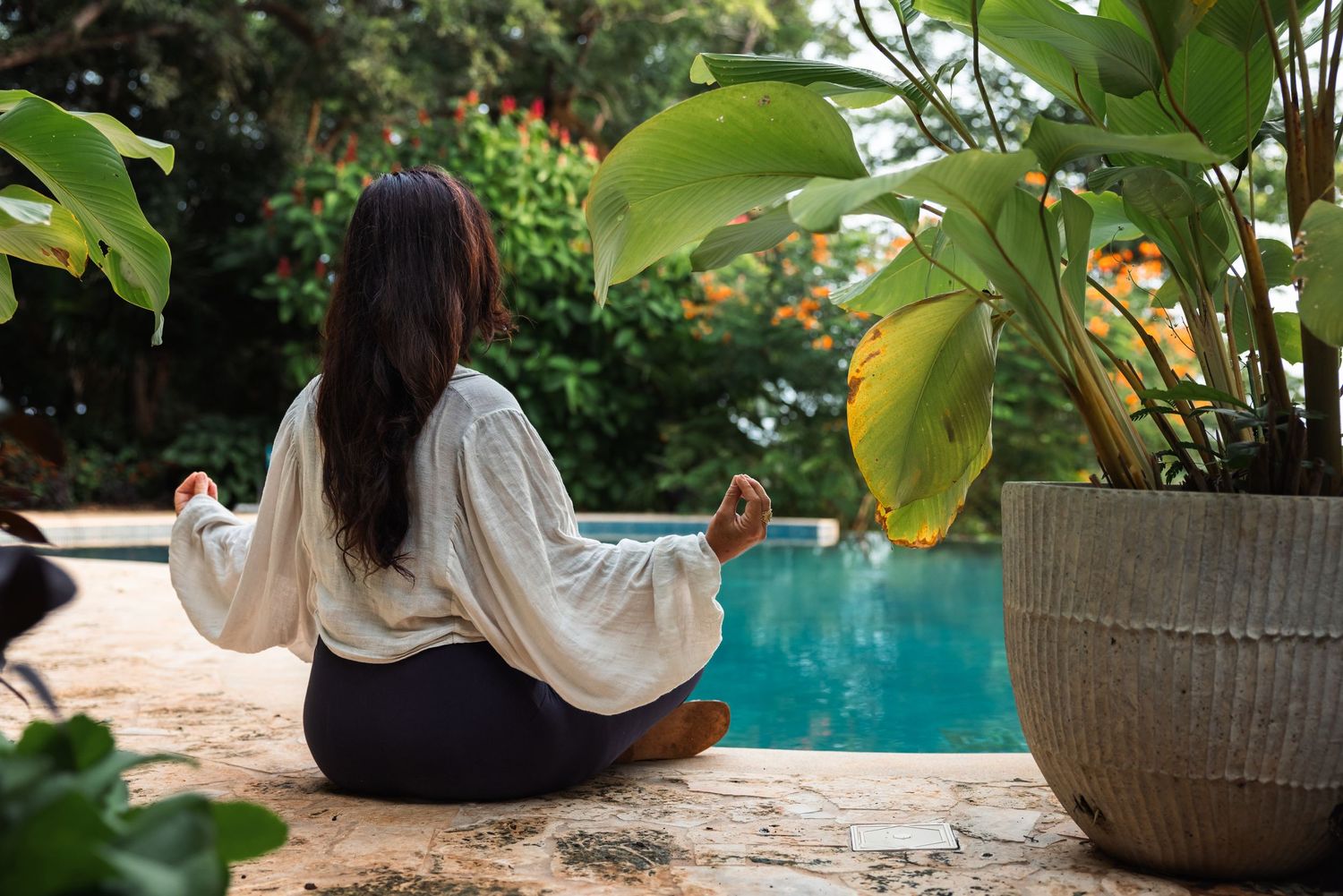 Peaceful poolside setting with tropical plants and woven furniture beside an infinity pool.