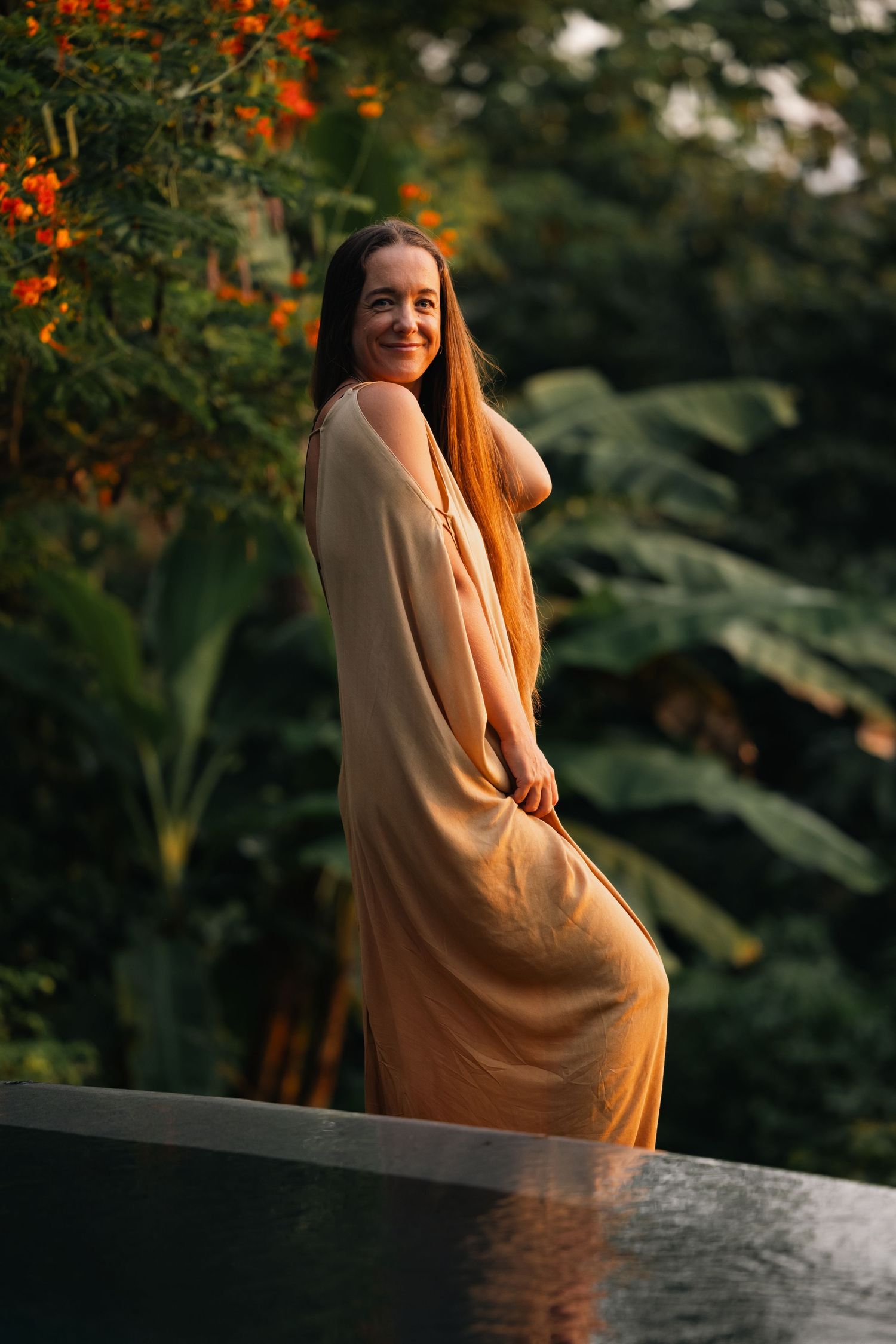 Elegant outdoor photoshoot featuring flowing peach dress against tropical garden backdrop.