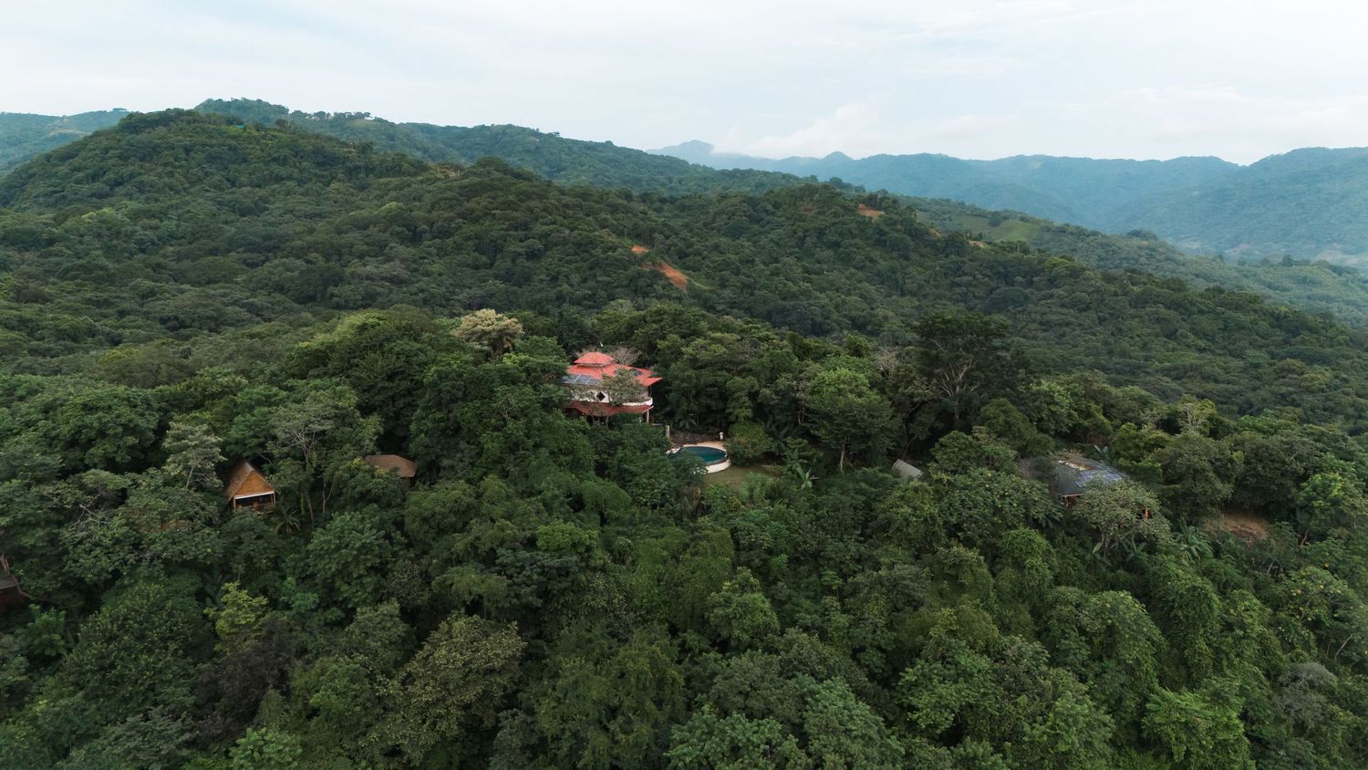 Sweeping mountain vista showing forested hillsides and scattered buildings in tropical setting.