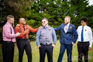 Groomsmen in suits and ties playfully pose together in an outdoor farm setting.