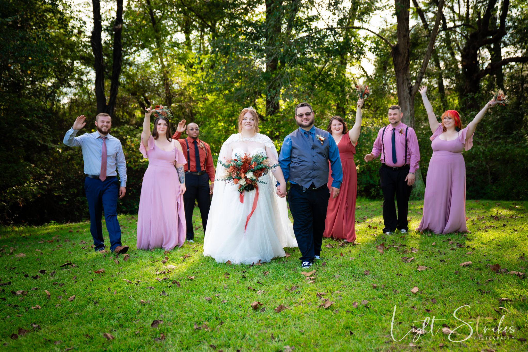 A wedding party stands in a lush green garden setting wearing in north Carolina outdoor farm wedding.