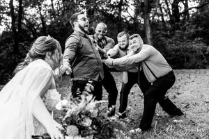 A wedding party having fun while groomsman dragging the groom from the bride in an outdoor farm wedding setting in North Carolina.
