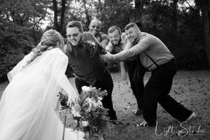 A wedding party having fun while groomsman dragging the groom from the bride in an outdoor farm wedding setting in North Carolina.