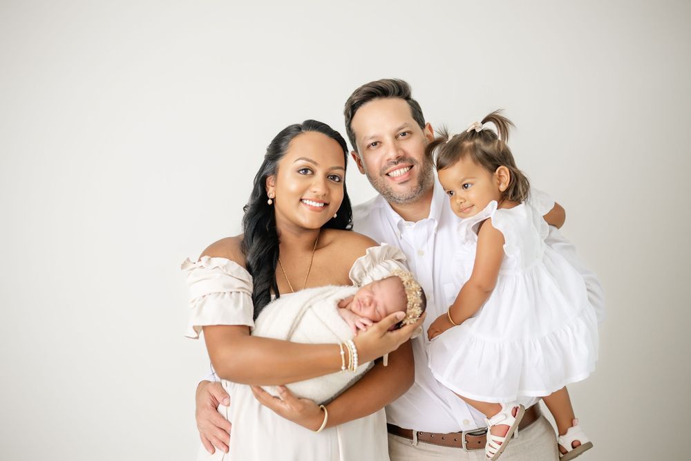 A family wearing white outfits poses together for a series of loving portraits against a light background.