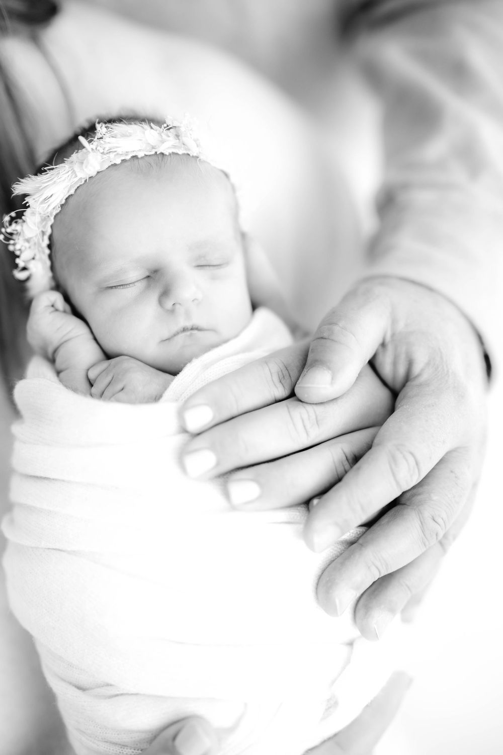 A series of black and white photographs showing a sleeping newborn baby wrapped in soft white blankets.