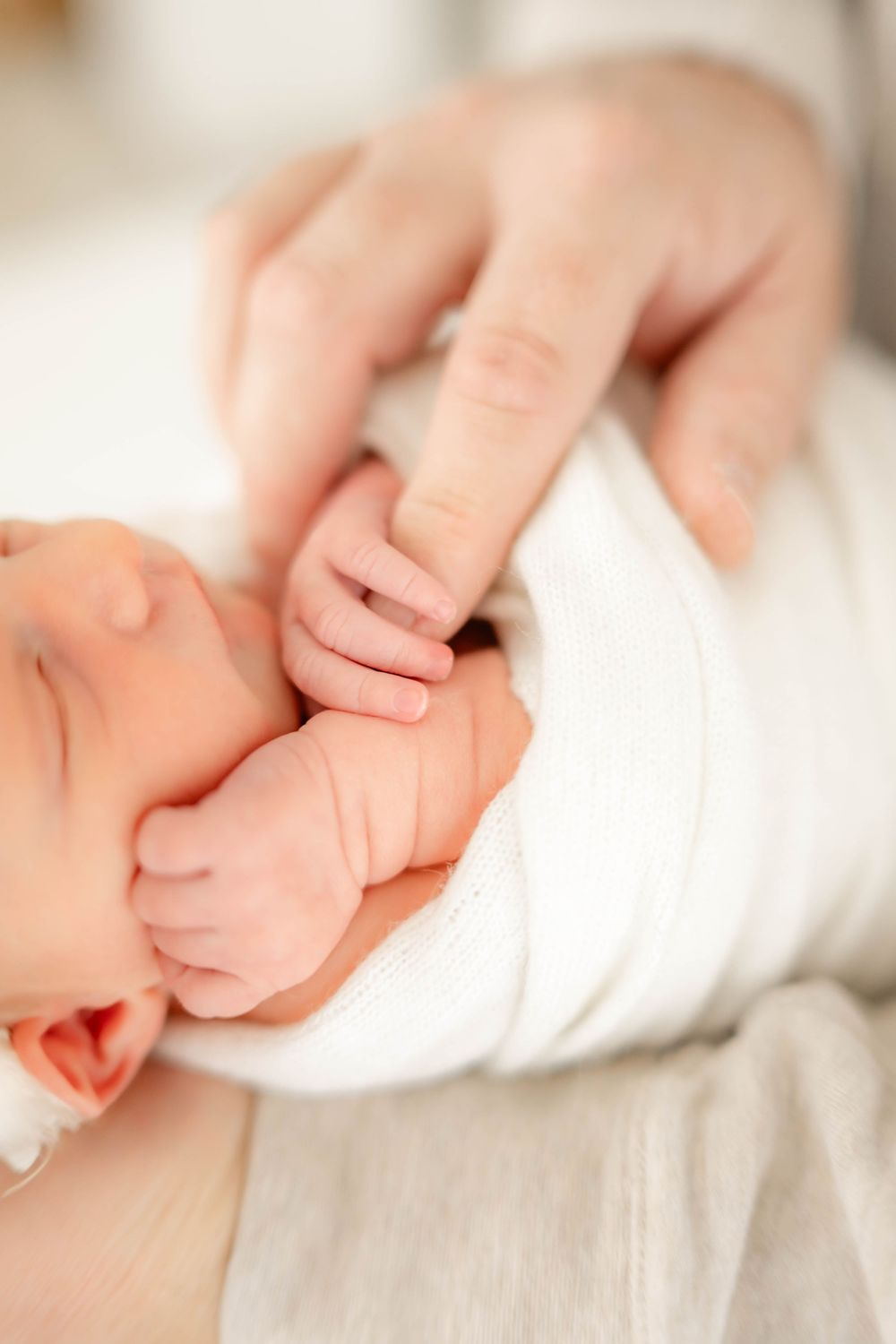 Close-up series of tiny newborn fingers grasping against soft white fabric.