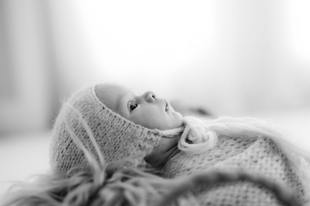 A sleeping baby wrapped in a cozy gray knit blanket rests peacefully in soft lighting.