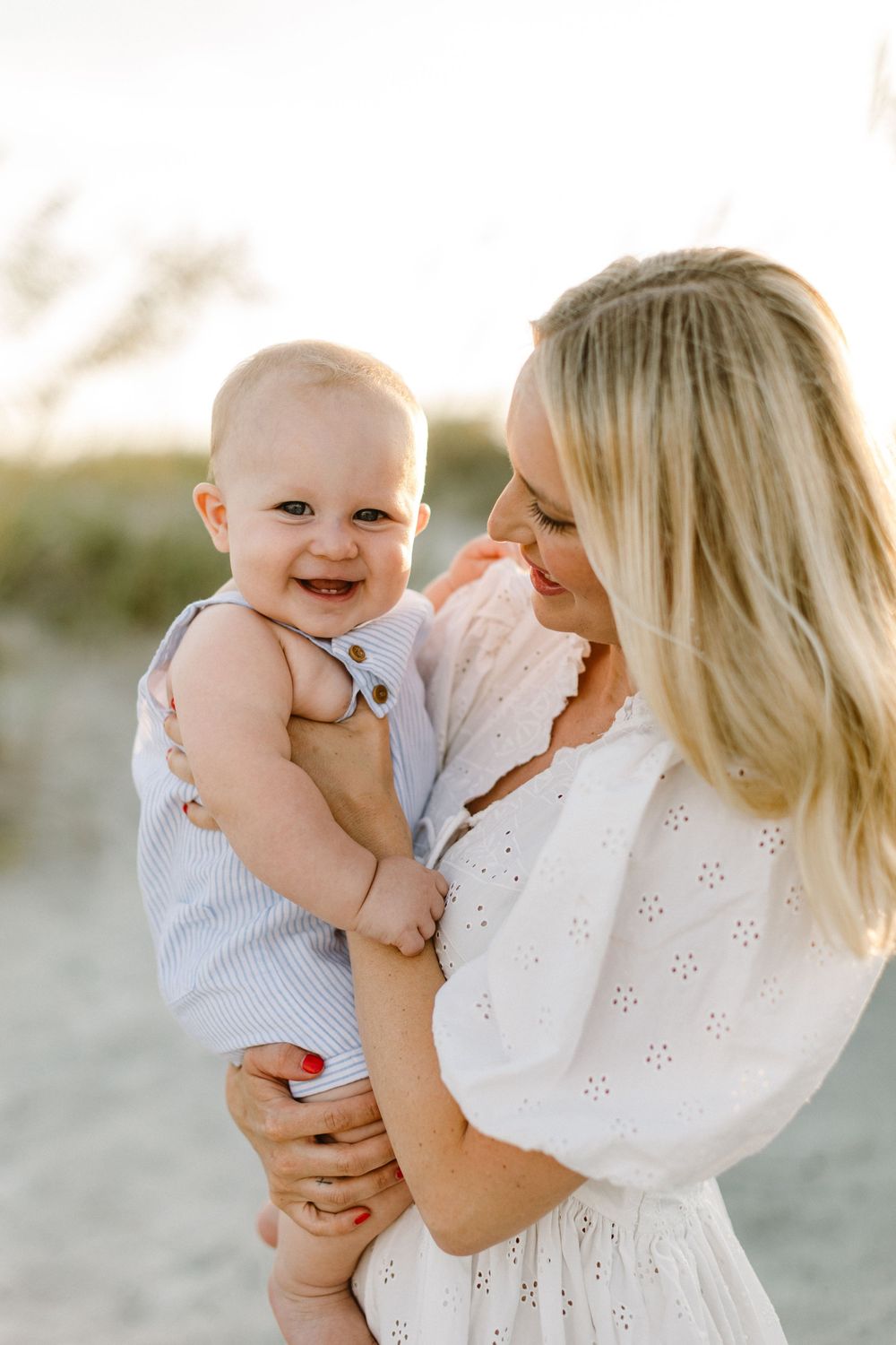 A tender moment captured in white outfits on a beach as a parent shares joyful interactions with a baby.
