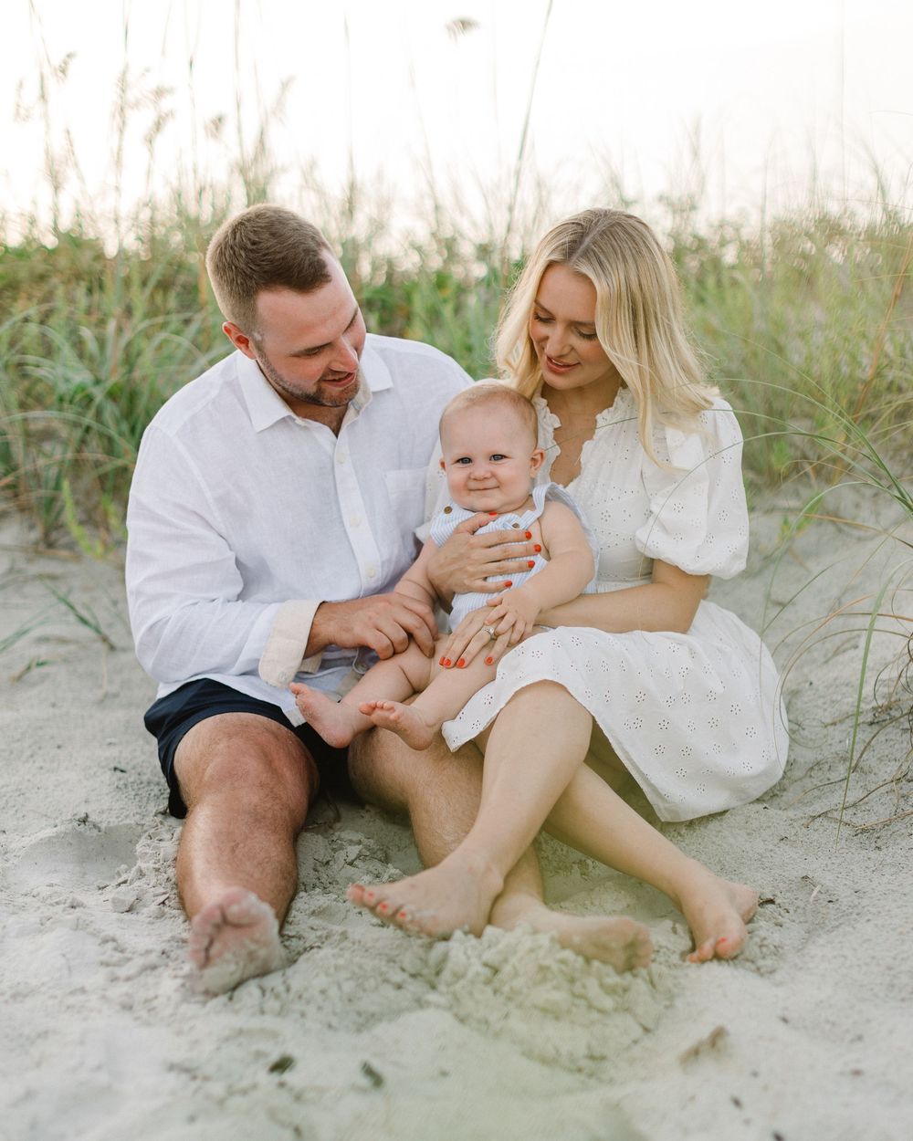 Family shares joyful moments together while sitting on sandy beach dunes during golden hour.