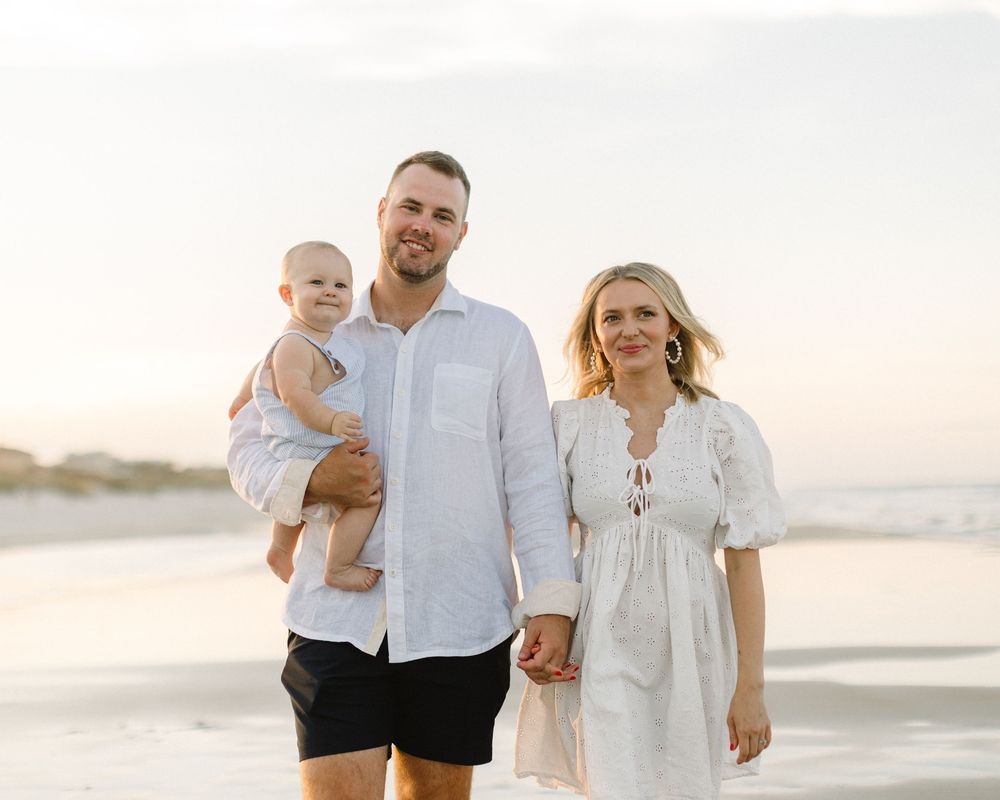 A family walks together on a sunny beach wearing white and light colored clothing during sunset.