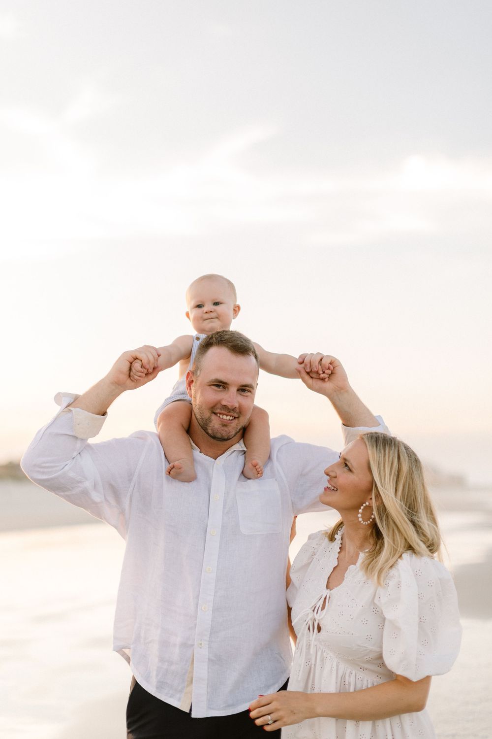 A couple dances joyfully on the beach wearing coordinated white outfits during a sunset photoshoot.