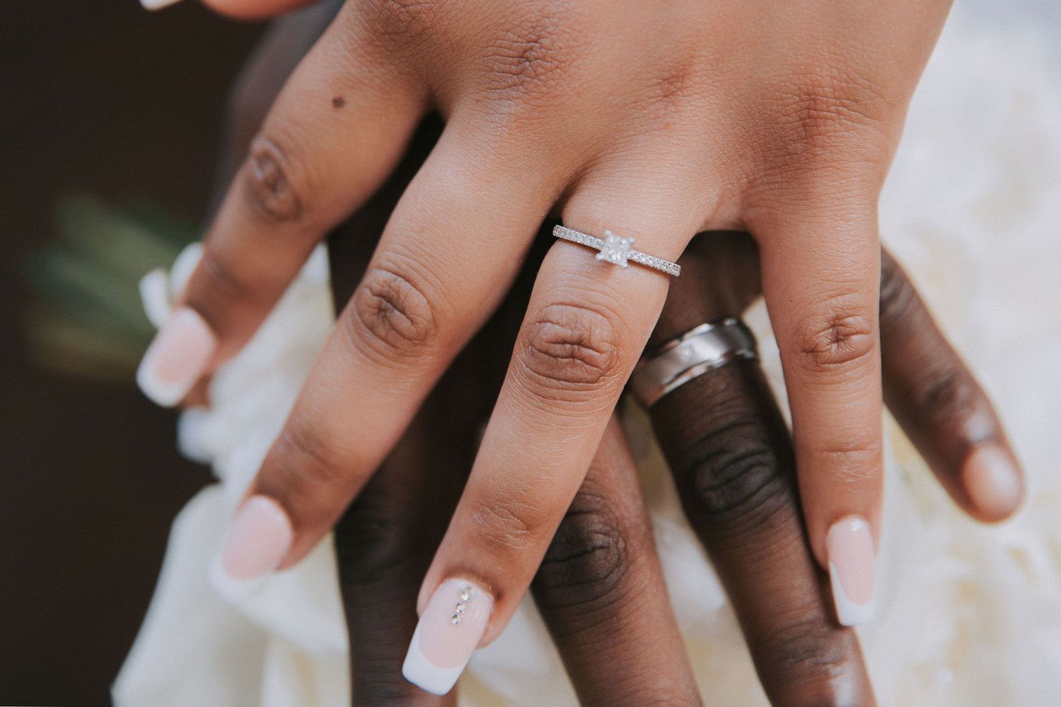 Close-up of hands showing off wedding rings against a blurred natural background.