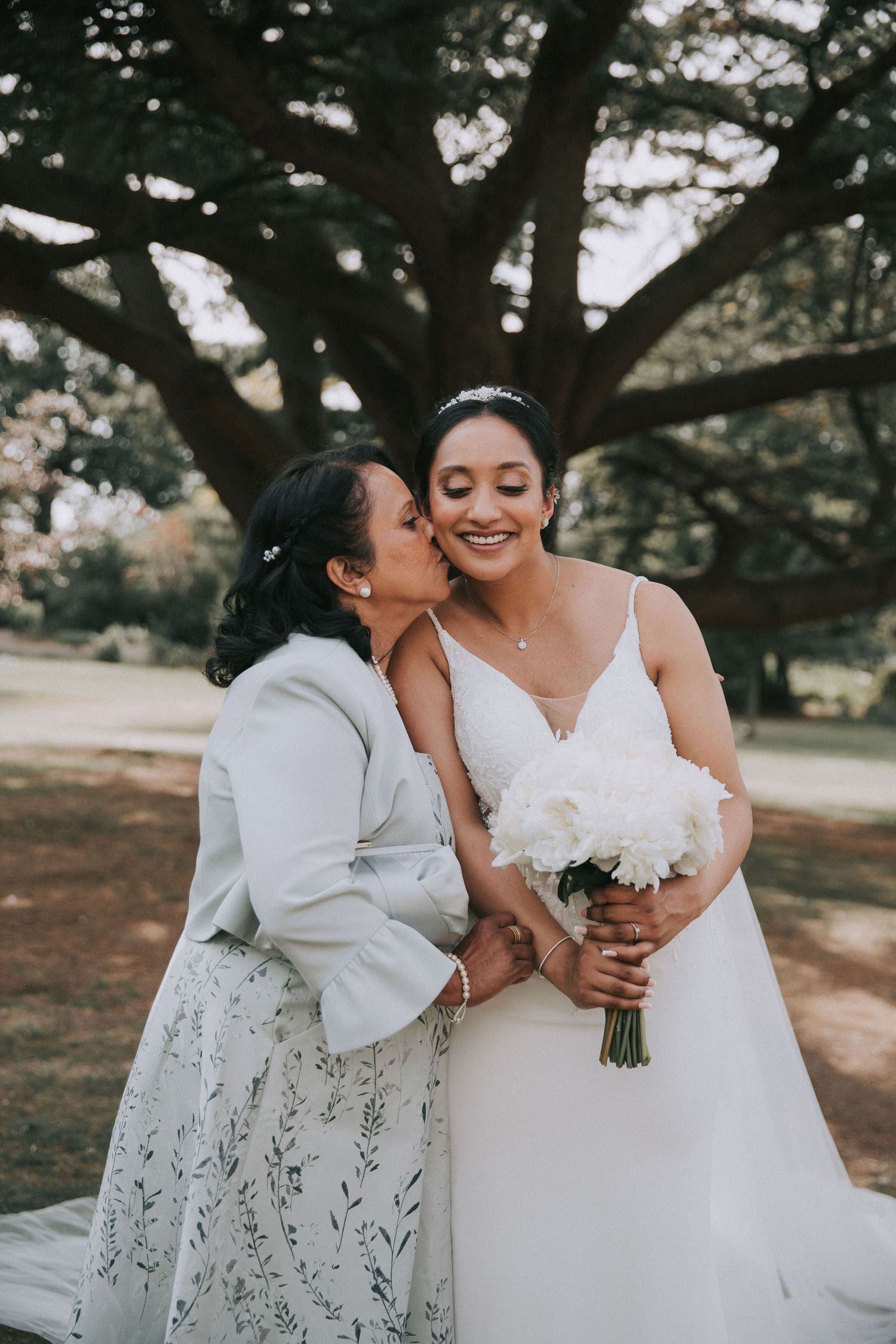 A tender moment between two people in wedding attire, with one wearing white and holding a bouquet of flowers.