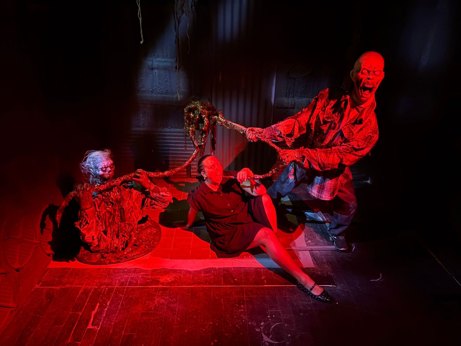 Performers dance and move dramatically under intense red lighting on a dark stage during a theatrical production.