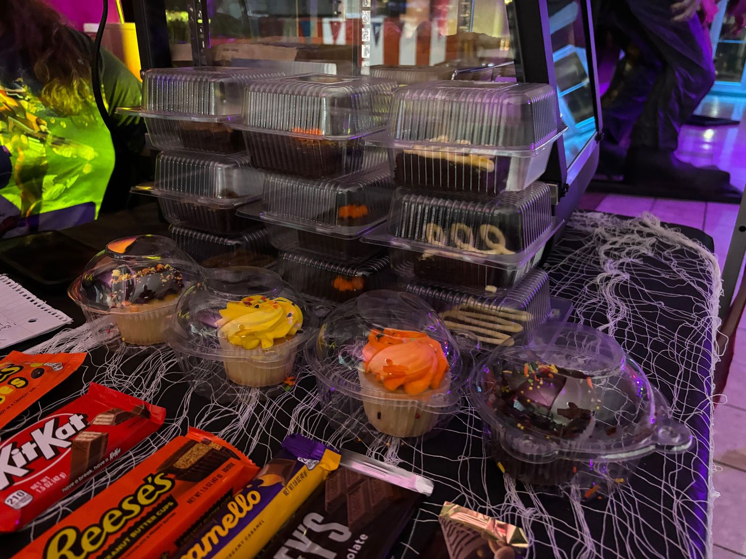 Halloween candy display with Kit Kats and spooky decorations illuminated by purple lighting at a party setup.
