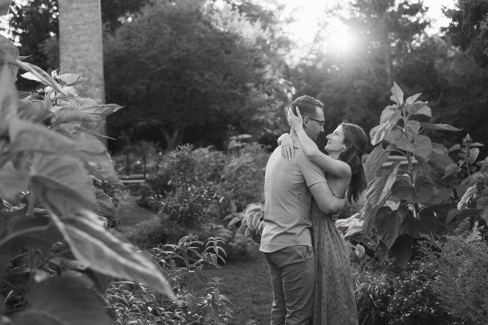 A couple dancing together in a garden setting during golden hour with sunlight filtering through trees.