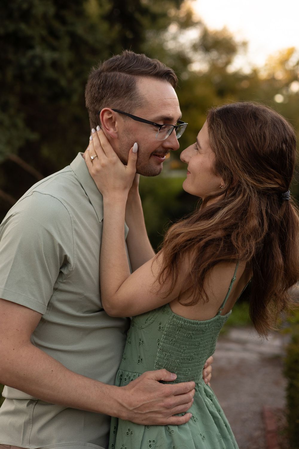 A romantic couple in matching sage green outfits share an intimate moment at sunset in an outdoor setting.