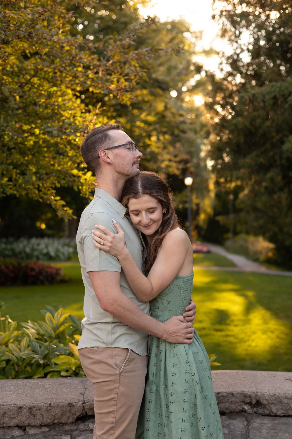 A couple embraces during a romantic sunset photoshoot in a park with golden light filtering through autumn trees.