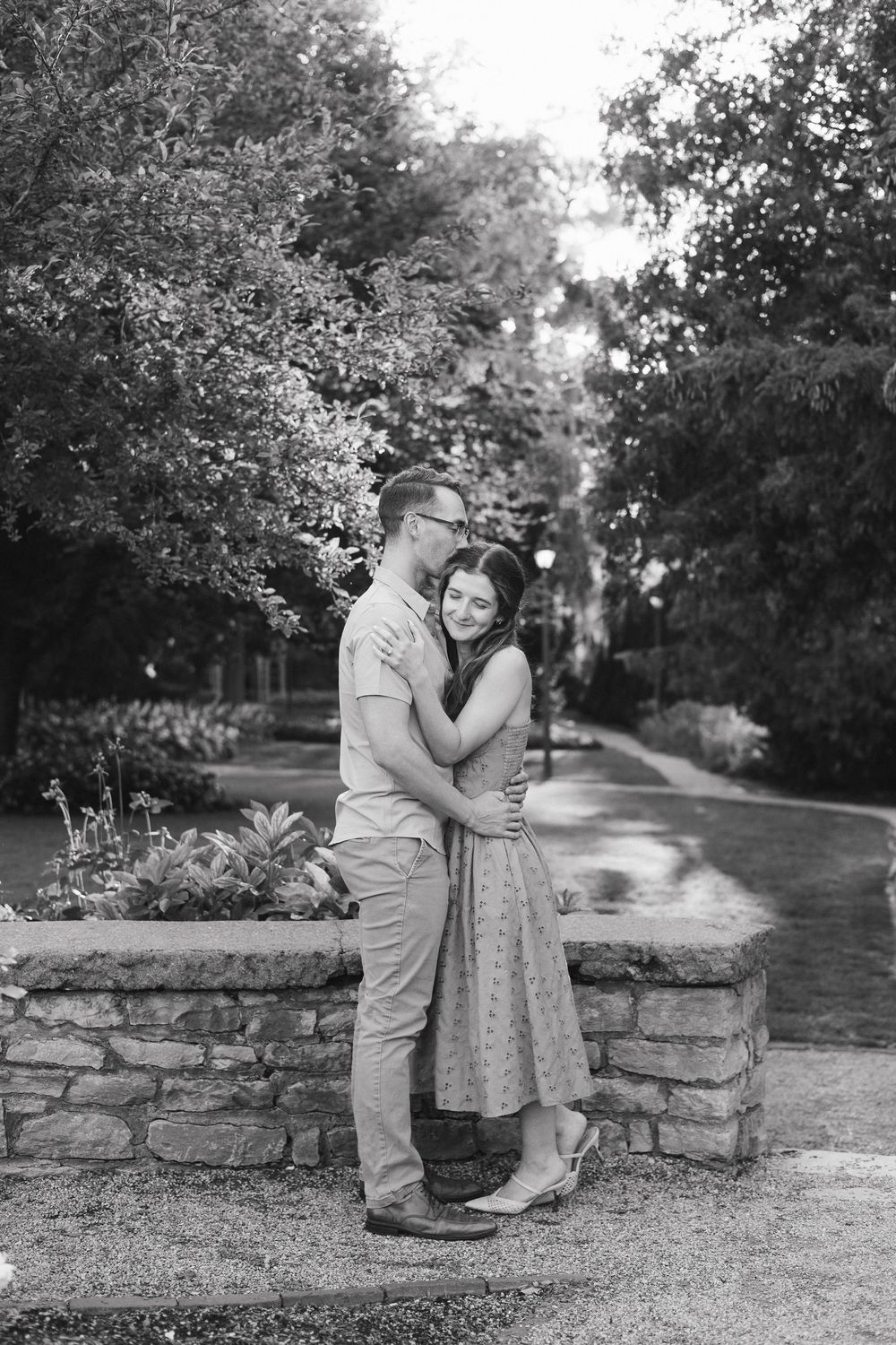 A couple shares a tender moment together on a rustic stone wall surrounded by lush greenery in a garden setting.
