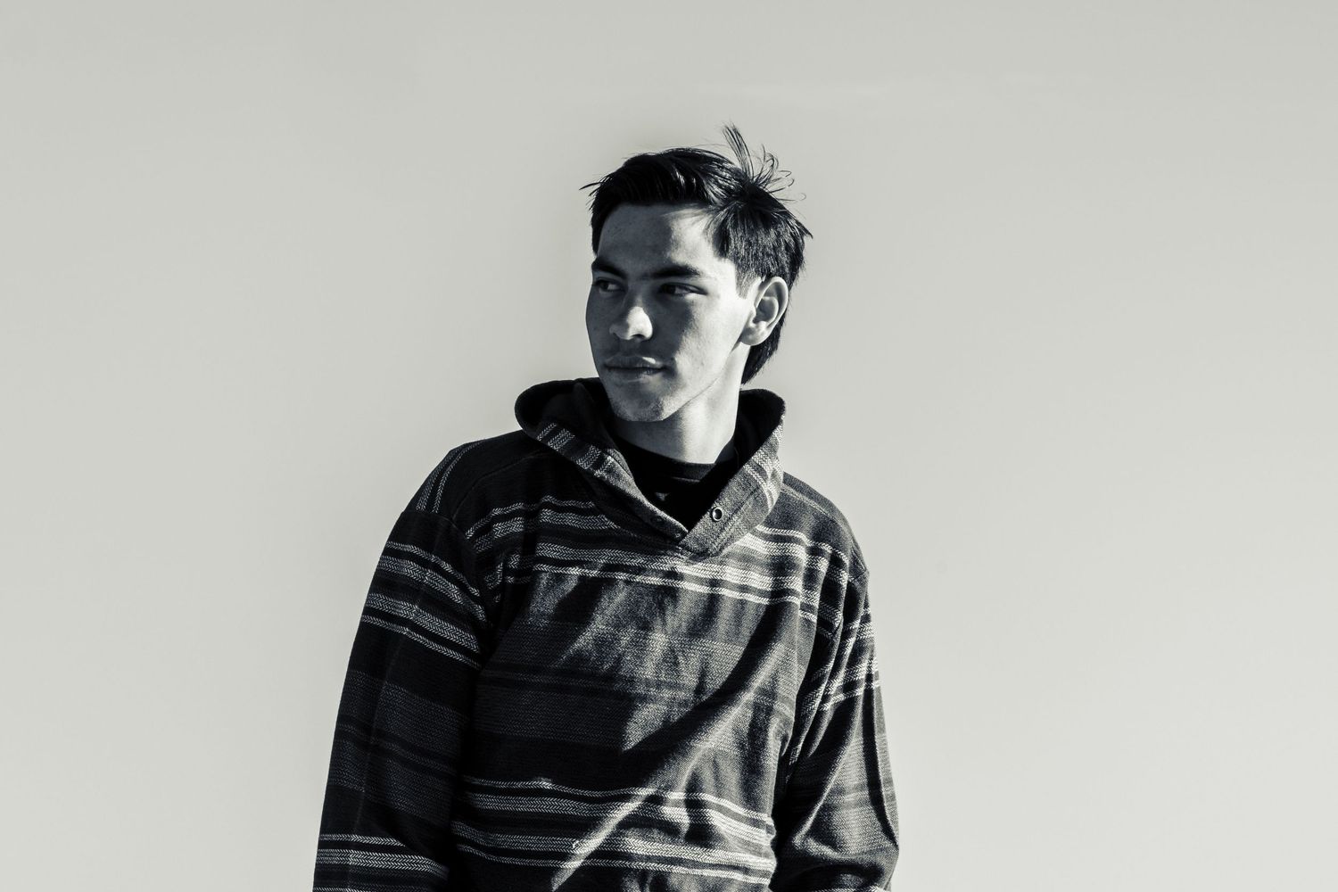 Young man in patterned hoodie poses against white wall in black and white portrait.