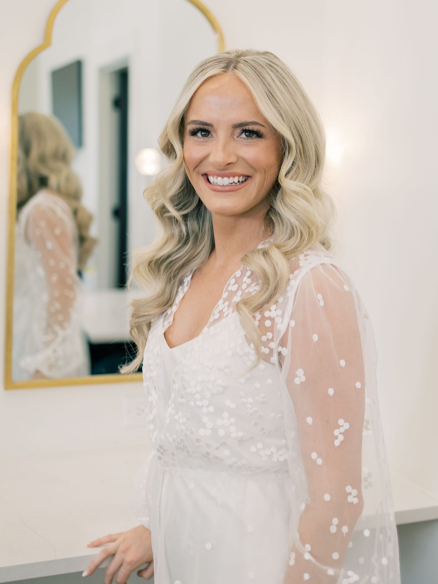 Bride wearing delicate white lace dress with sheer sleeves in bright natural light setting.