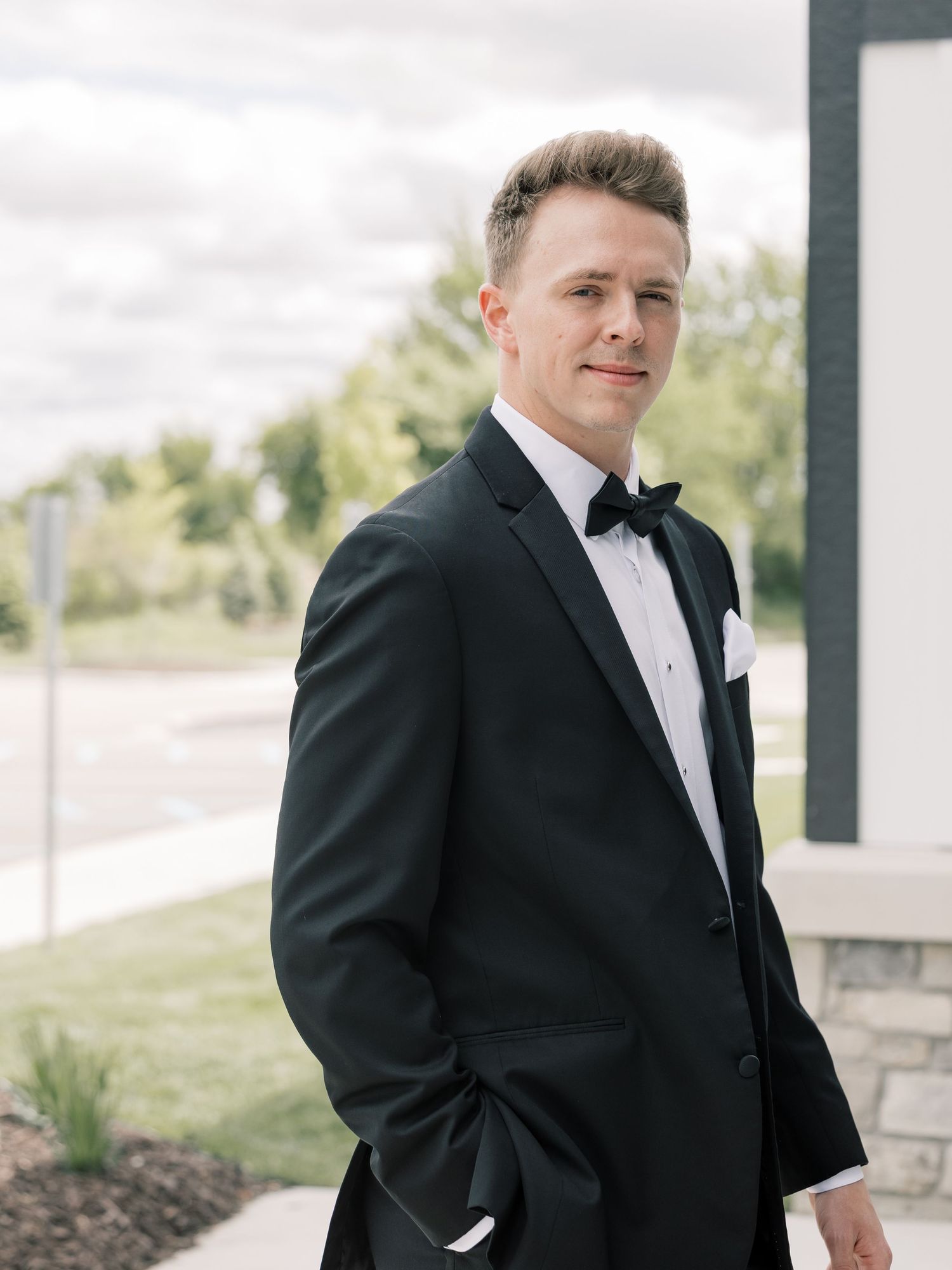 Groom in classic black tuxedo poses for formal wedding portraits outdoors.