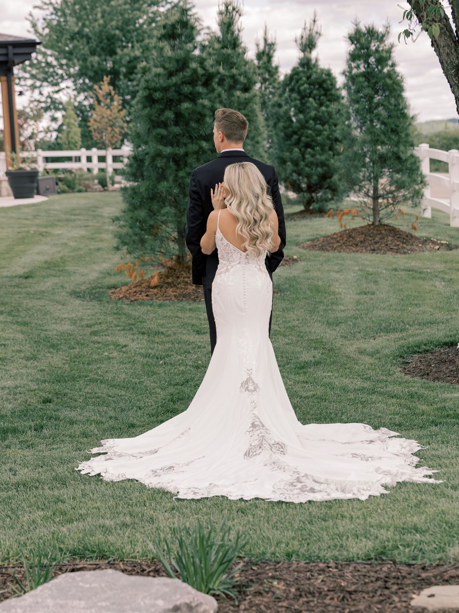 Beautiful lace wedding dress with a flowing train photographed outdoors on green grass.