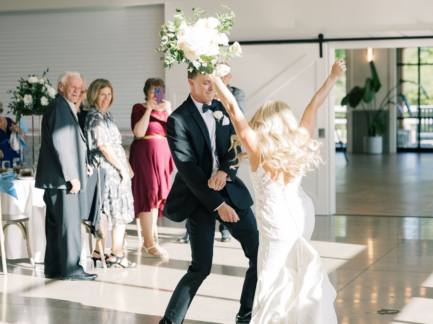 Wedding reception celebration with guests dancing in a bright modern venue.