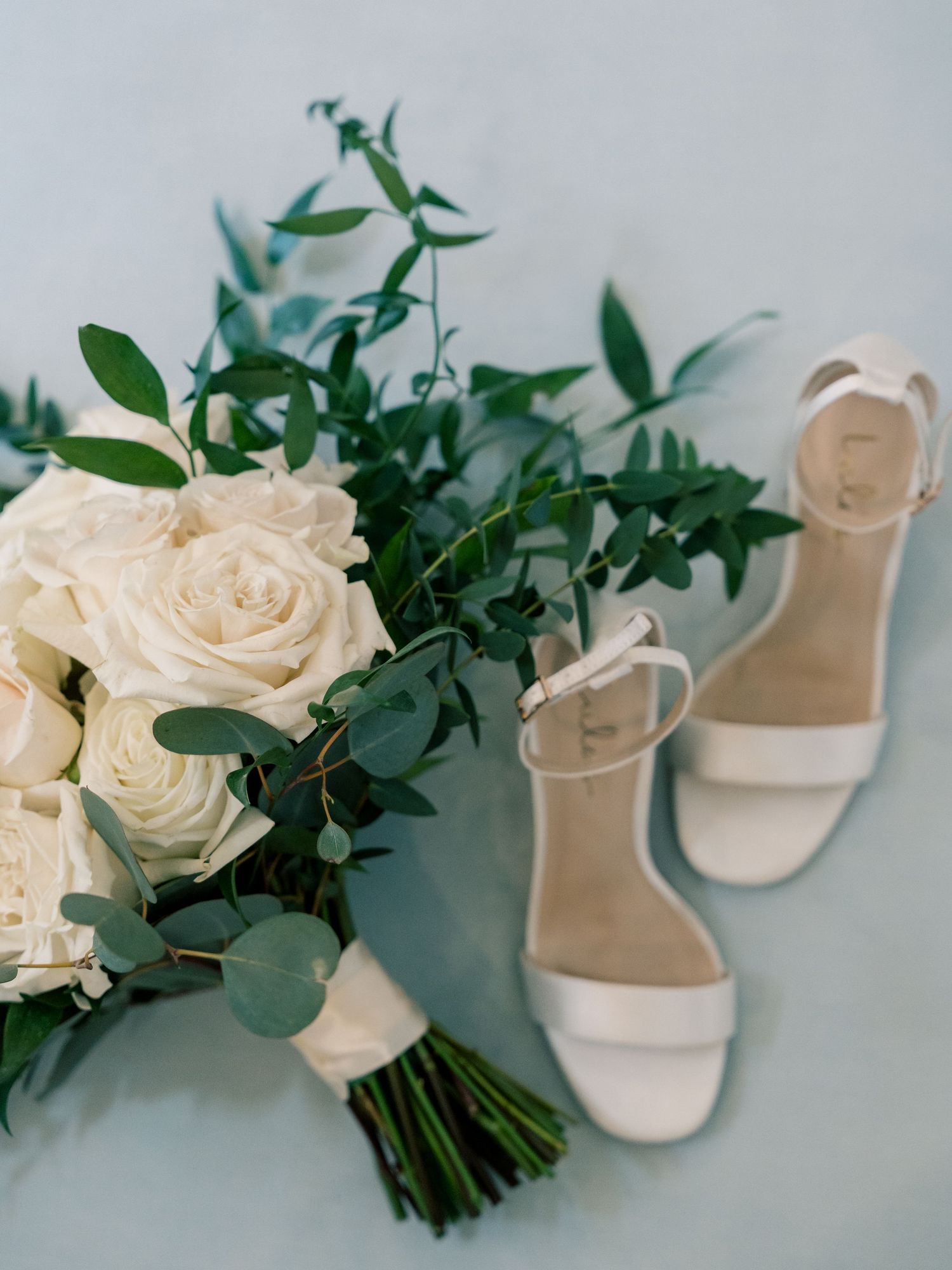 White roses and eucalyptus wedding bouquet styled with bridal shoes.