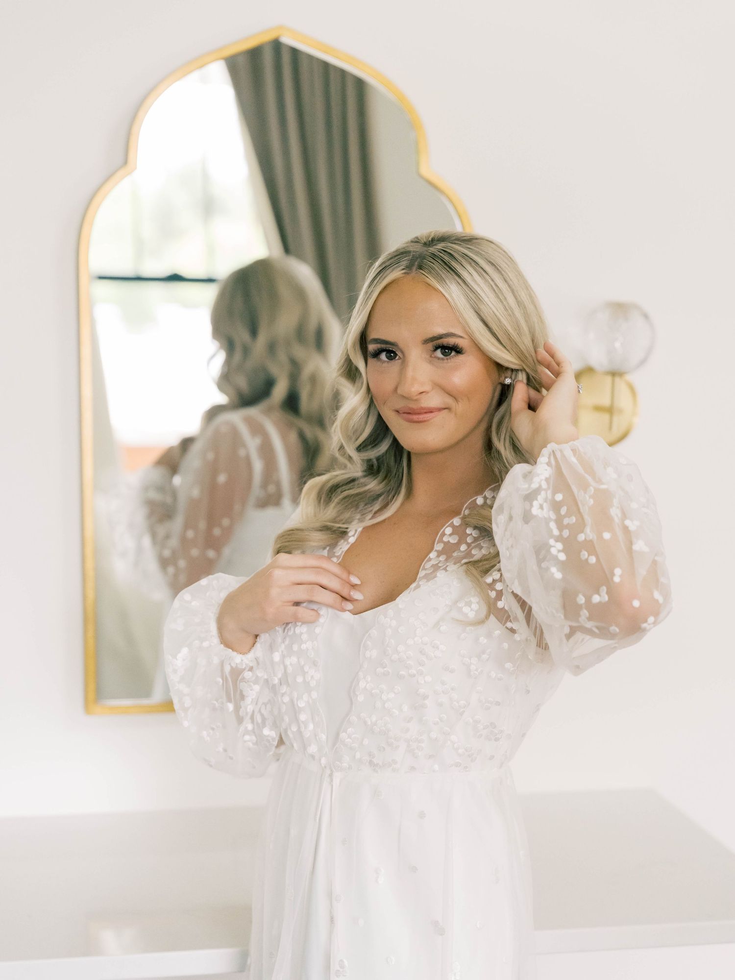 Bridal preparation in elegant white room with gold-framed mirrors.