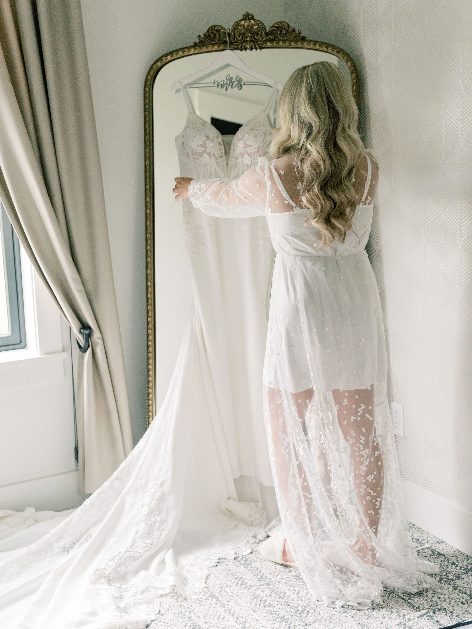 Ethereal bridal gown with lace details photographed in soft window light with vintage mirror.