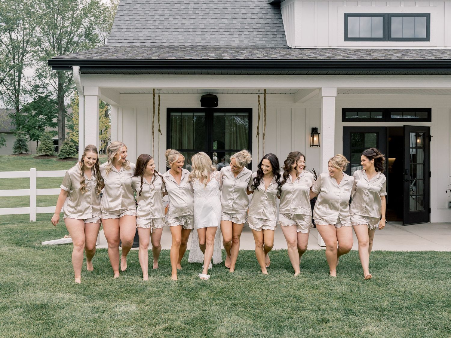 Bridesmaids sitting in a row showing off their bare legs in matching robes outside a house.