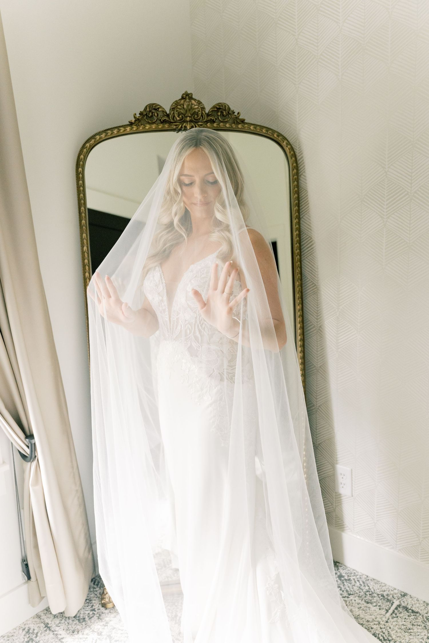 Bridal veil and dress captured in dreamy window light with ornate gold mirror reflection.