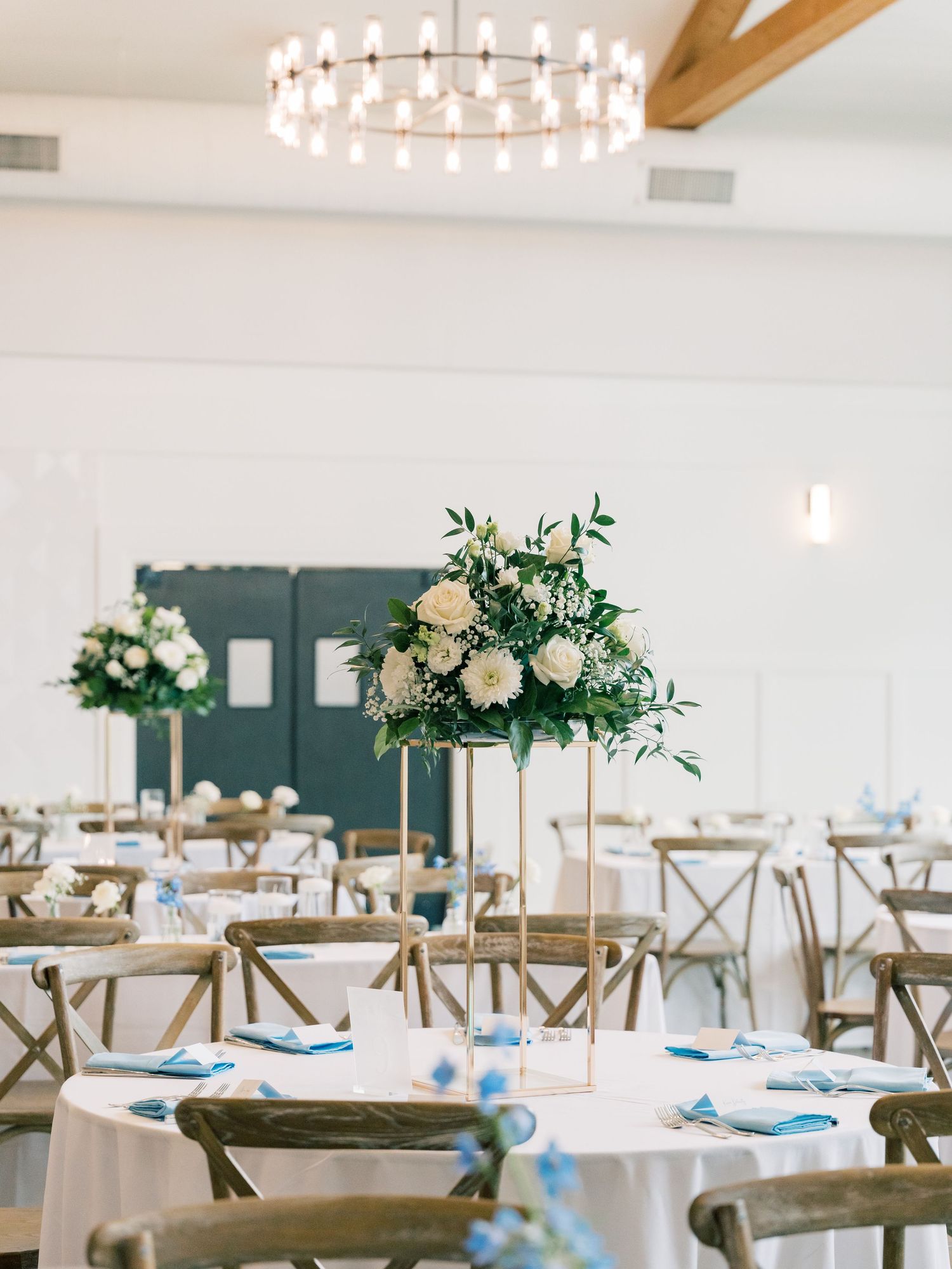 Modern wedding reception setup with wooden chairs and elegant floral centerpieces.