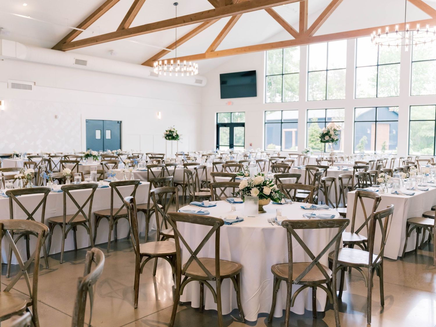 Modern white wedding reception venue with wooden cross-back chairs and exposed beams.