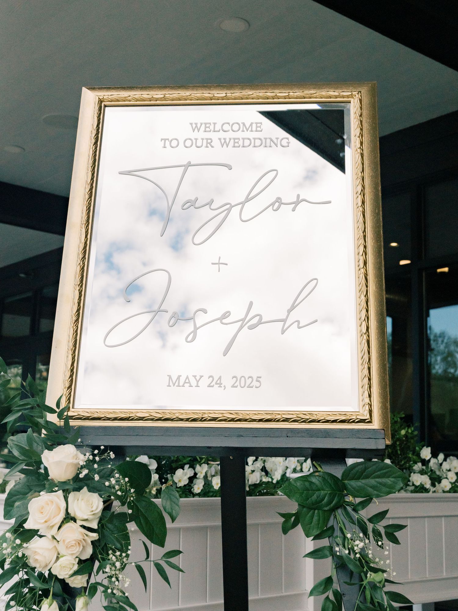 Wedding welcome sign with floral garland and elegant gold frame.