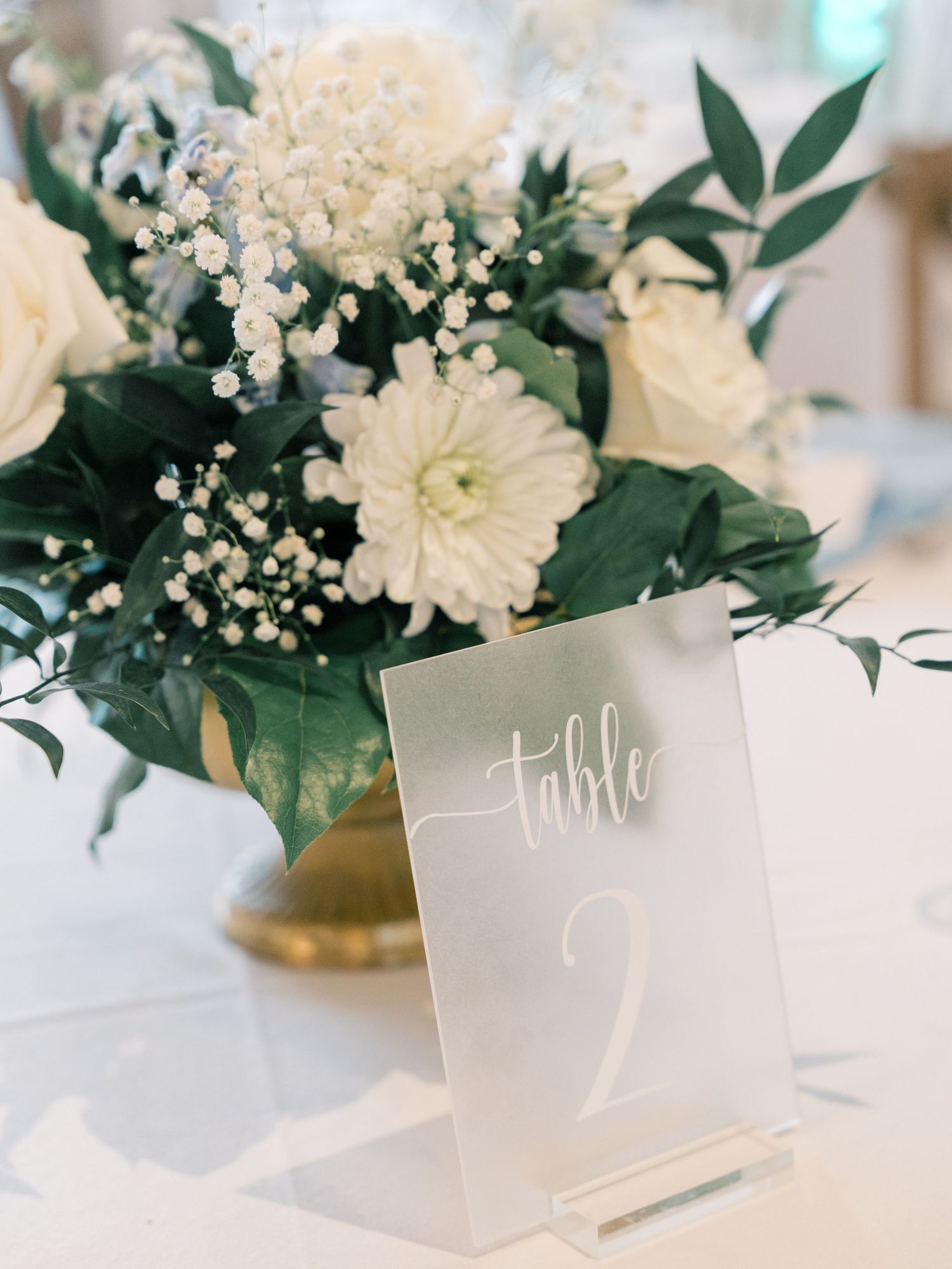 Elegant wedding table settings with white floral centerpieces and handwritten table number cards.