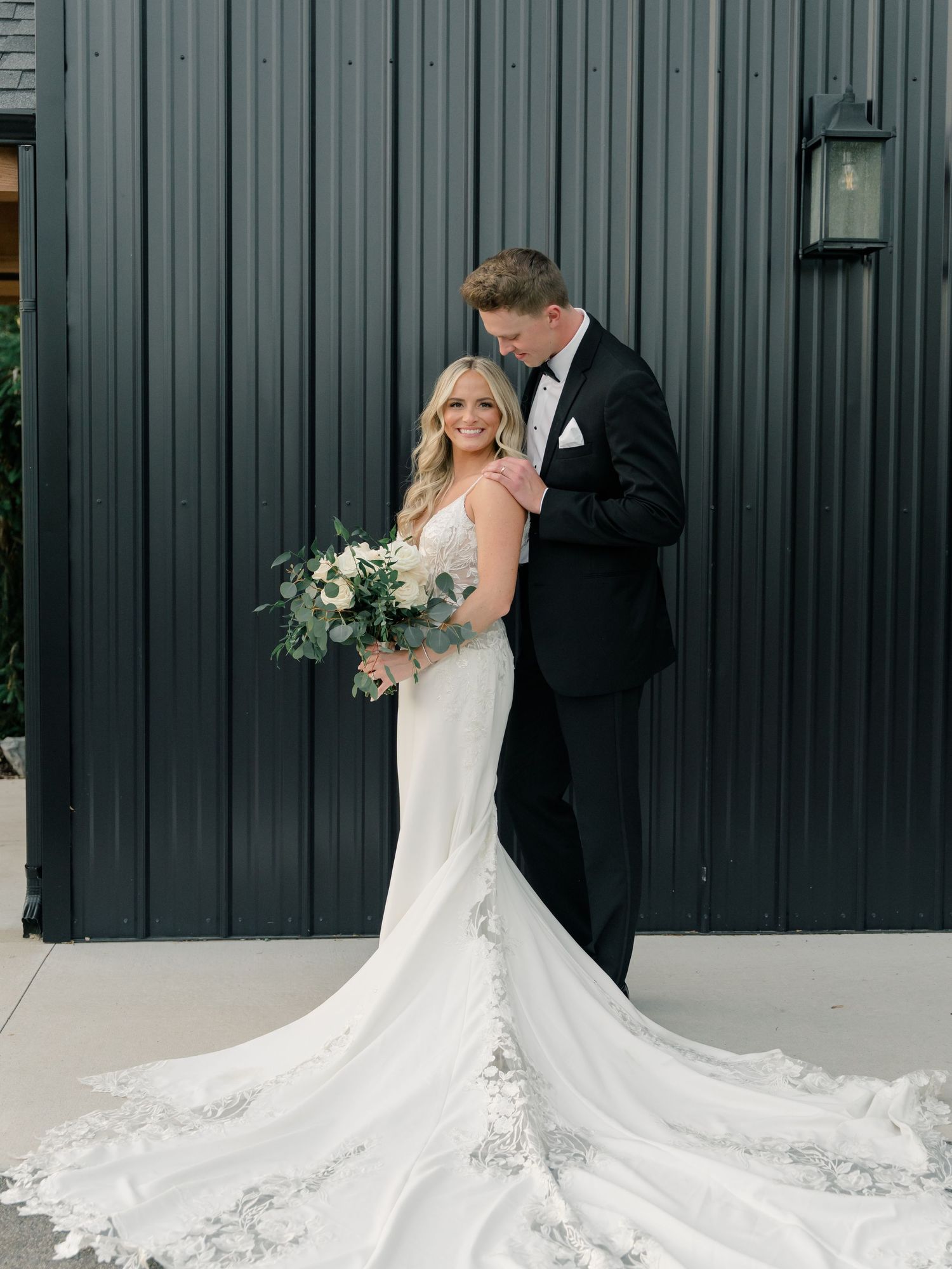 A stunning white lace wedding dress with cathedral train against dark modern building.
