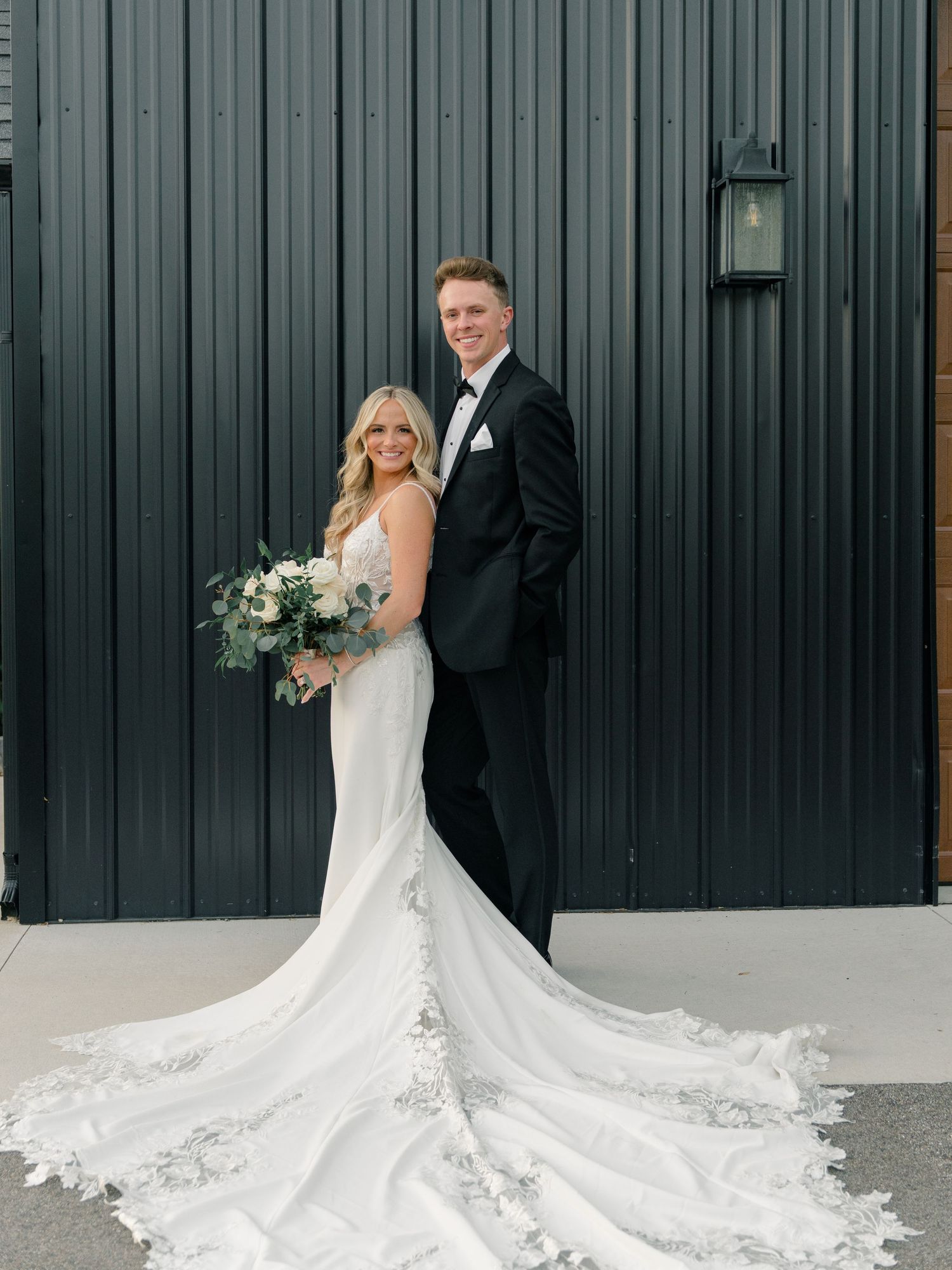 An elegant bridal portrait showcasing a flowing white lace gown against a dark modern backdrop.