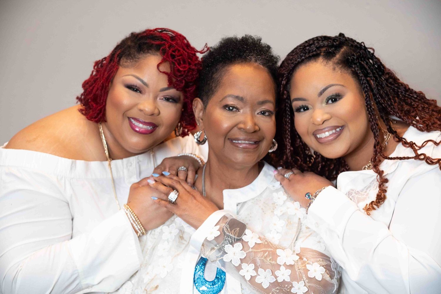 Three women in white outfits smile warmly while posing together for a group photo.
