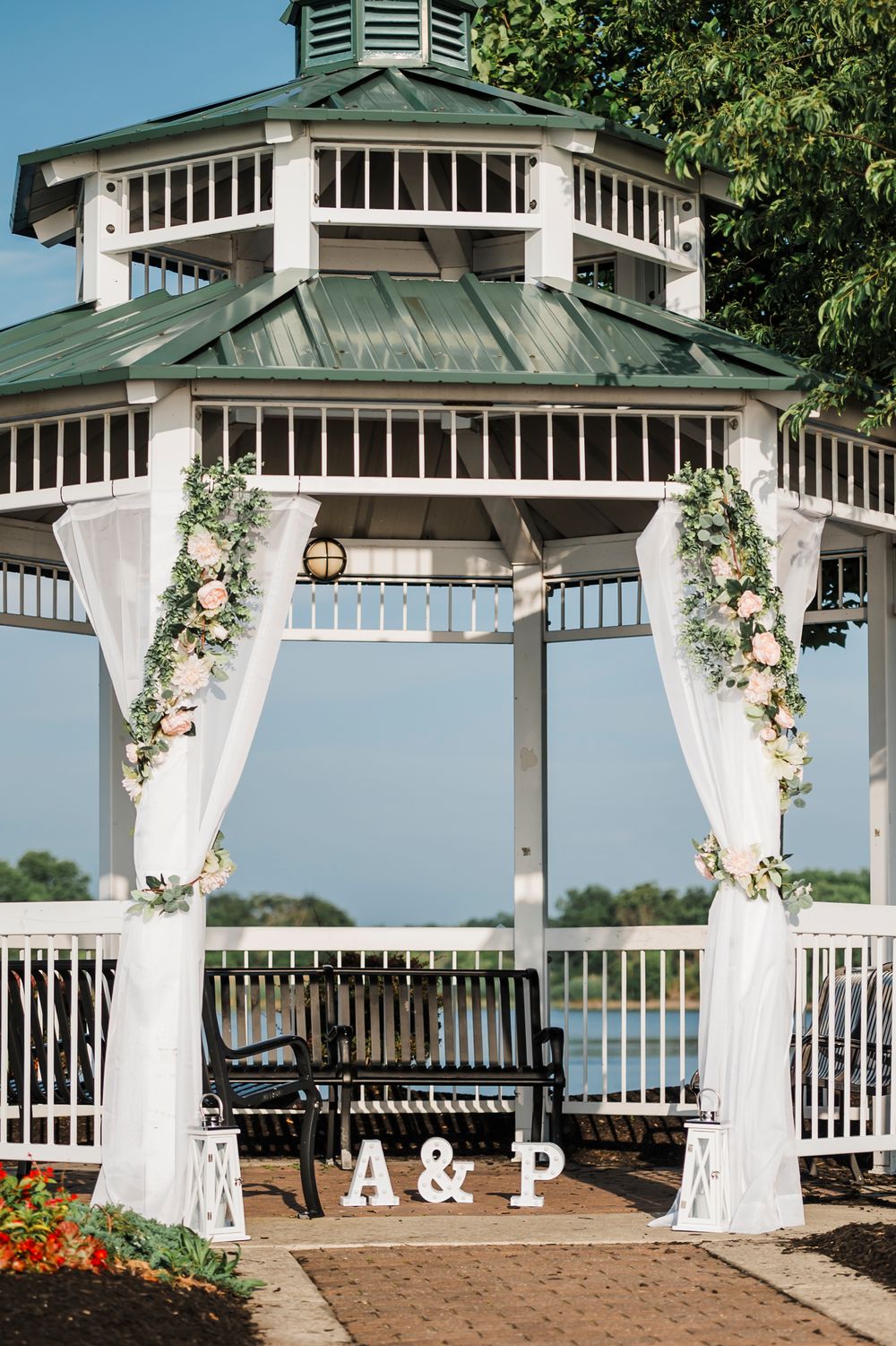 Elegant white gazebo decorated with floral garlands and sheer fabric overlooking a waterfront venue for a wedding ceremony.